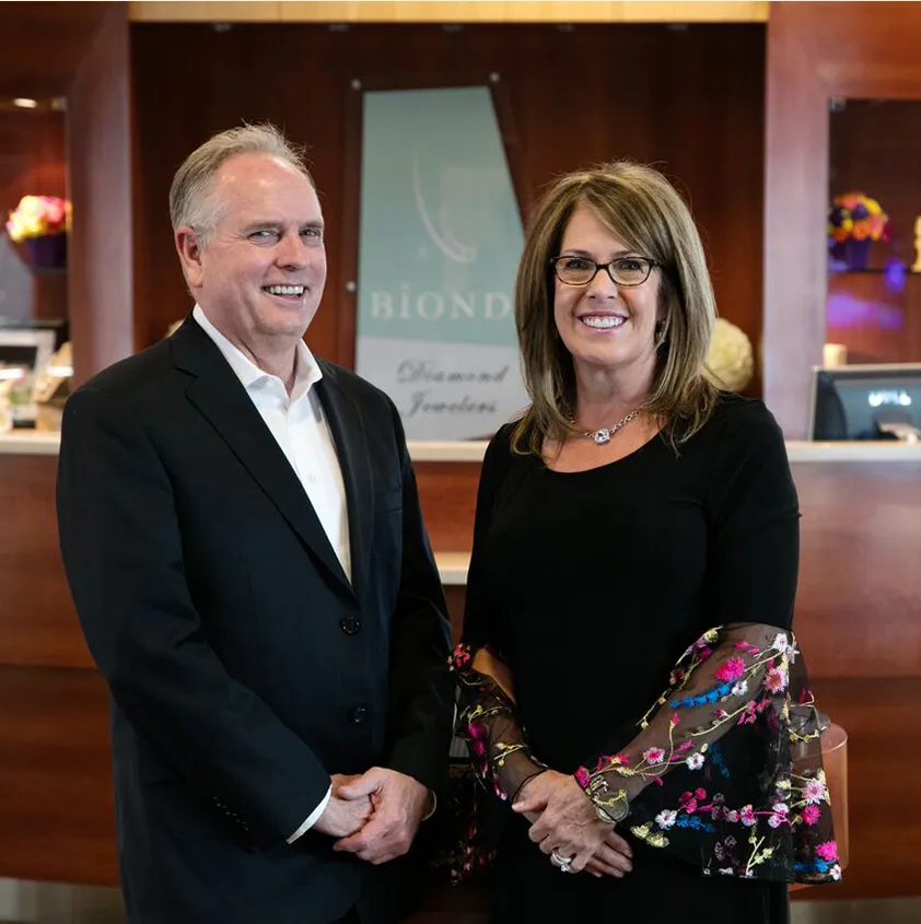 Owners standing in front of jewelry case inside Biondi Diamond Jewelers located in Aurora, CO