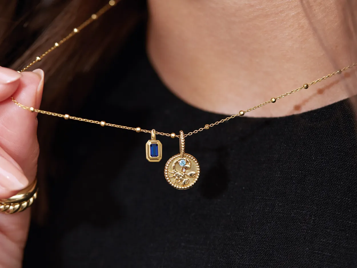 Gold necklace with two pendants: a blue stone and a decorative round charm, worn by a person.