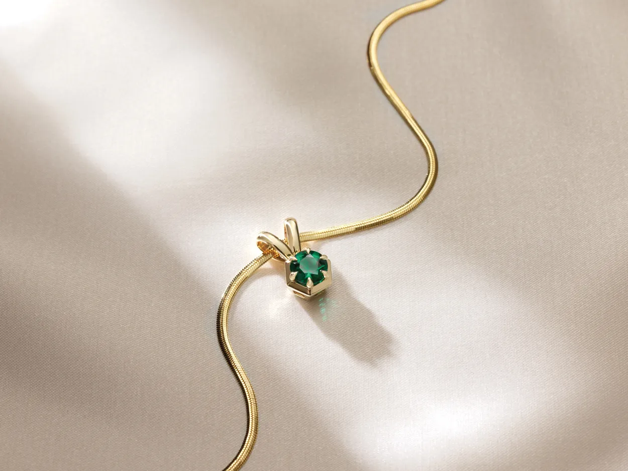 Gold necklace with a green gemstone pendant on a soft fabric background.