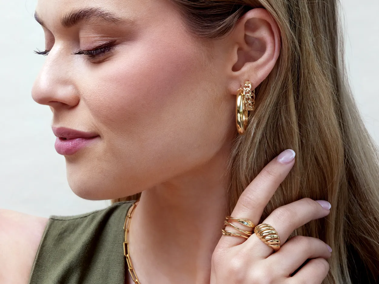 Close-up of a woman wearing gold hoop earrings and rings, showcasing elegant jewelry.