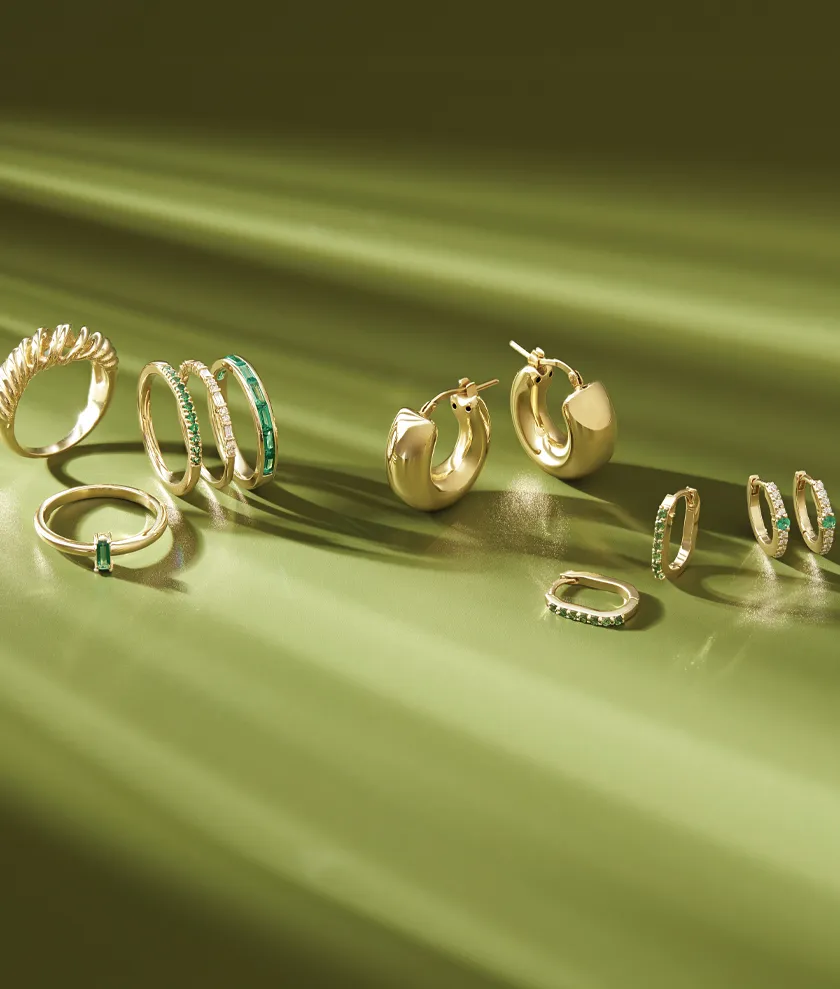 Gold earrings and rings with emerald accents displayed on a green background. 