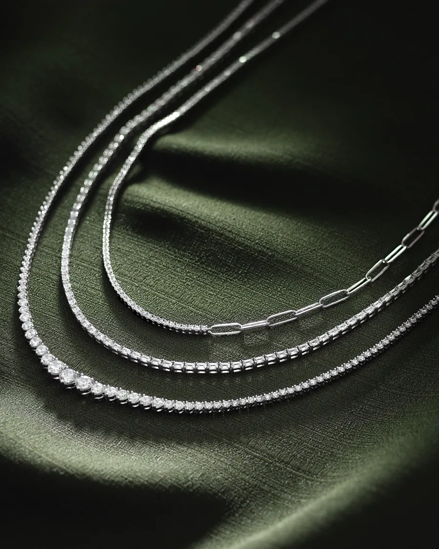 Elegant silver chains displayed on a dark green fabric background. 