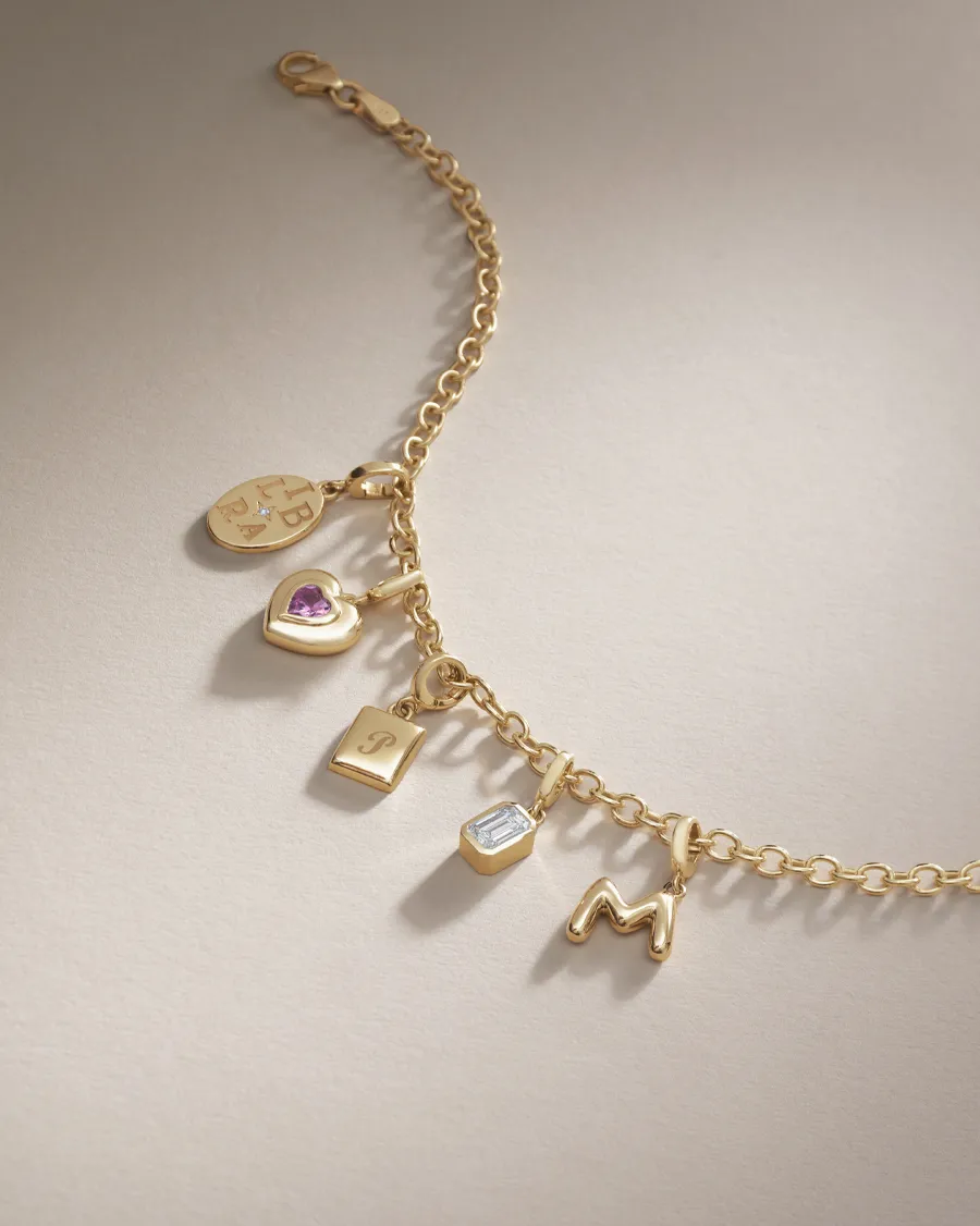 Gold charm bracelet featuring various charms including letters and a heart.
