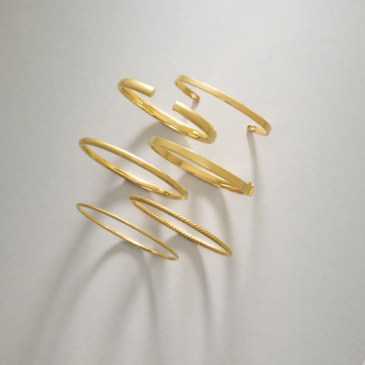 Six elegant gold bangles arranged artistically on a light background, showcasing various designs and styles.