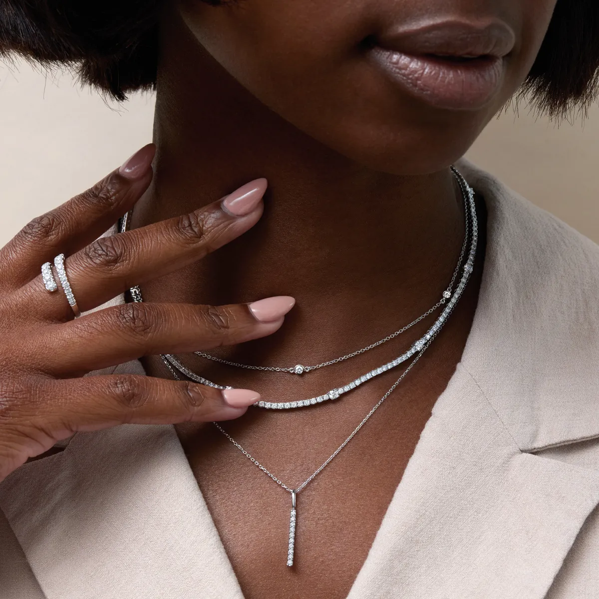 Close-up of a woman wearing layered silver necklaces and a diamond ring, showcasing elegant jewelry.