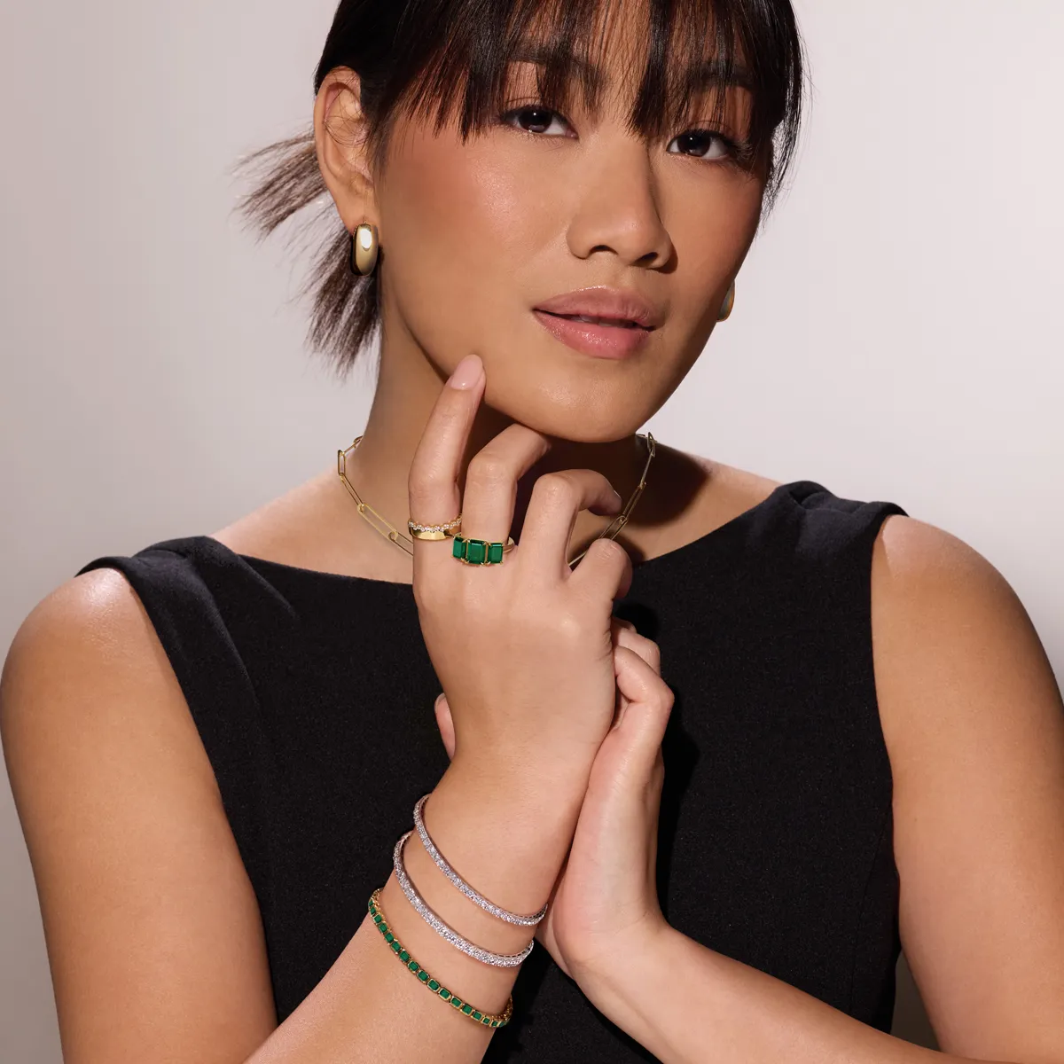 Model showcasing elegant jewelry, including green gemstones and gold accents, against a neutral background.