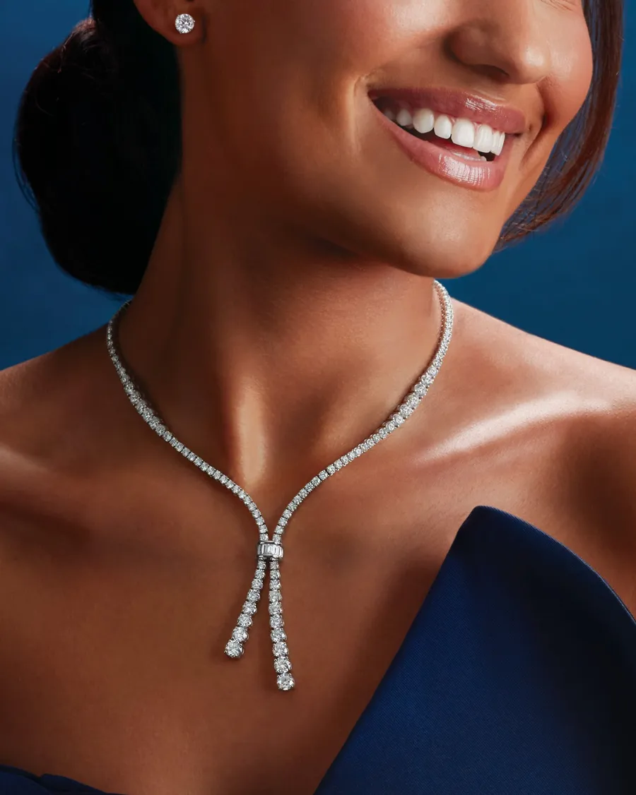 Elegant woman wearing a diamond necklace and earrings, smiling against a blue background.