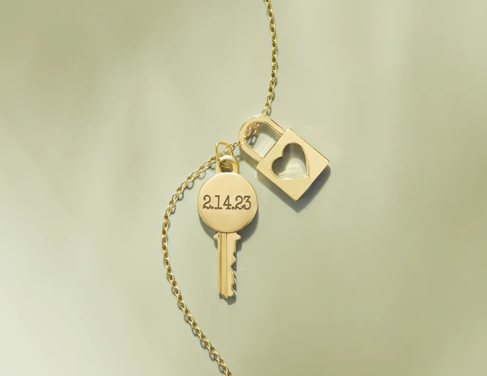 Gold necklace featuring a key and heart-shaped padlock charm, engraved with the date 2.14.23. Perfect for personalized jewelry.