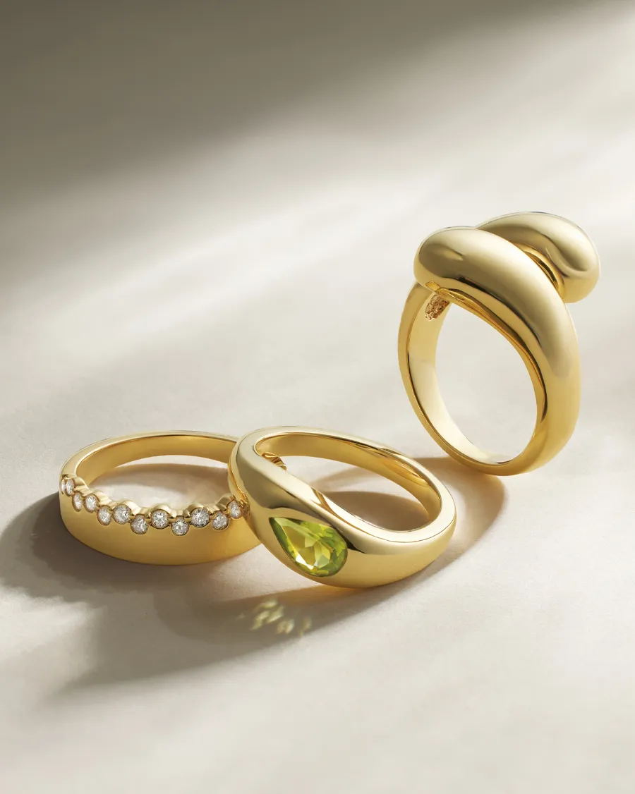 Three elegant gold rings featuring diamonds and a green gemstone, displayed on a soft surface. Click to Shop Now at 47thStreet.D