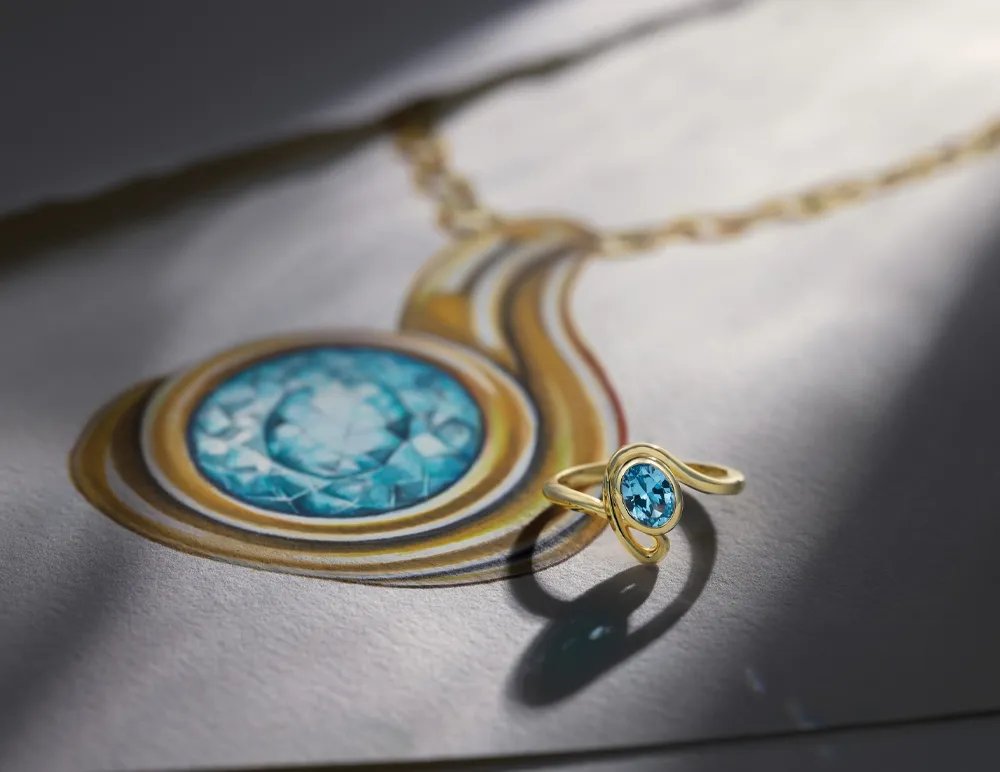 Gold ring with blue gemstone beside a drawing of a matching pendant necklace on a textured surface.