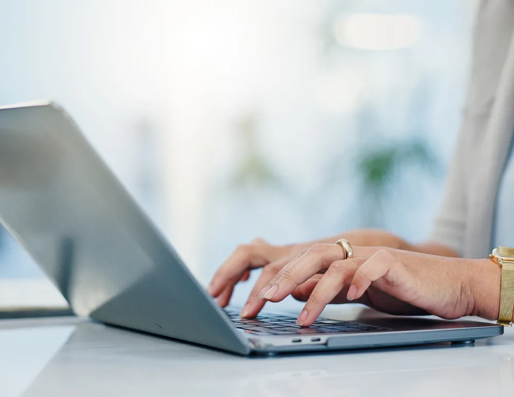 Person typing on a laptop in a bright, modern workspace, promoting virtual appointments.