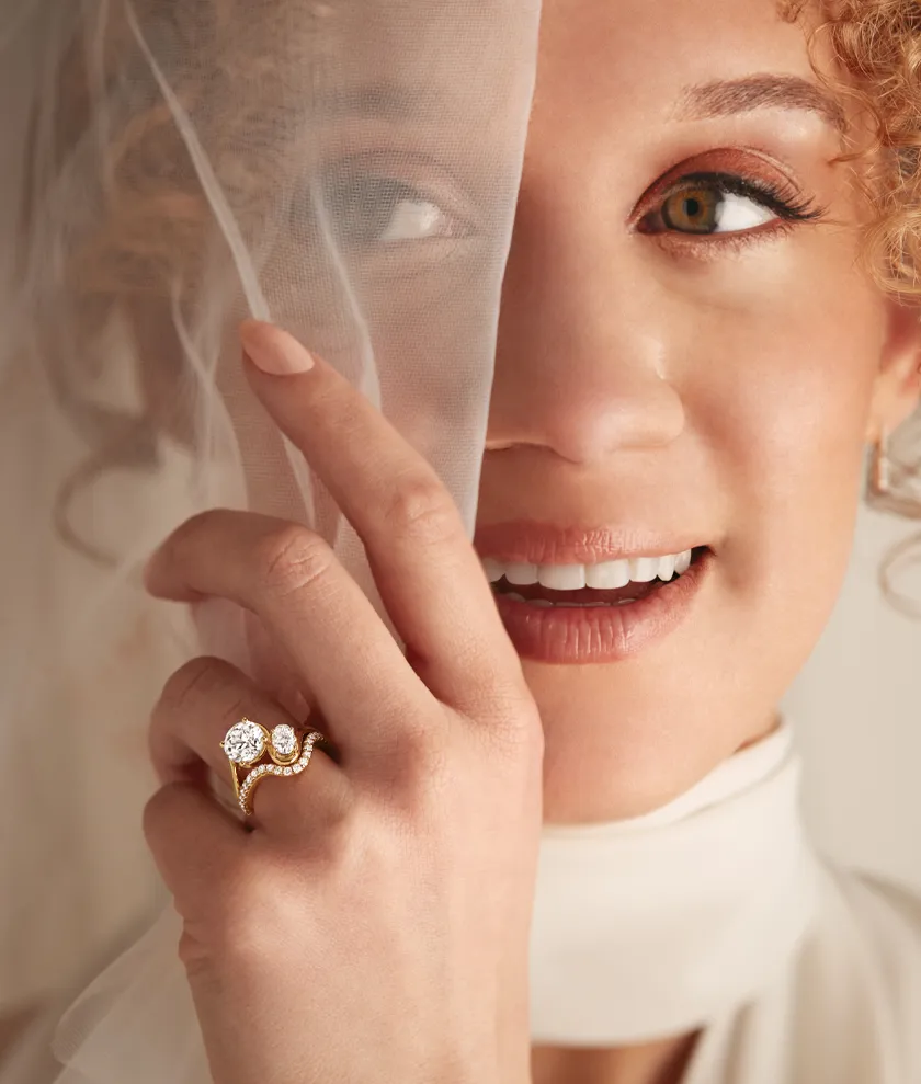 Bride smiling behind a veil, showcasing a stunning engagement ring. 