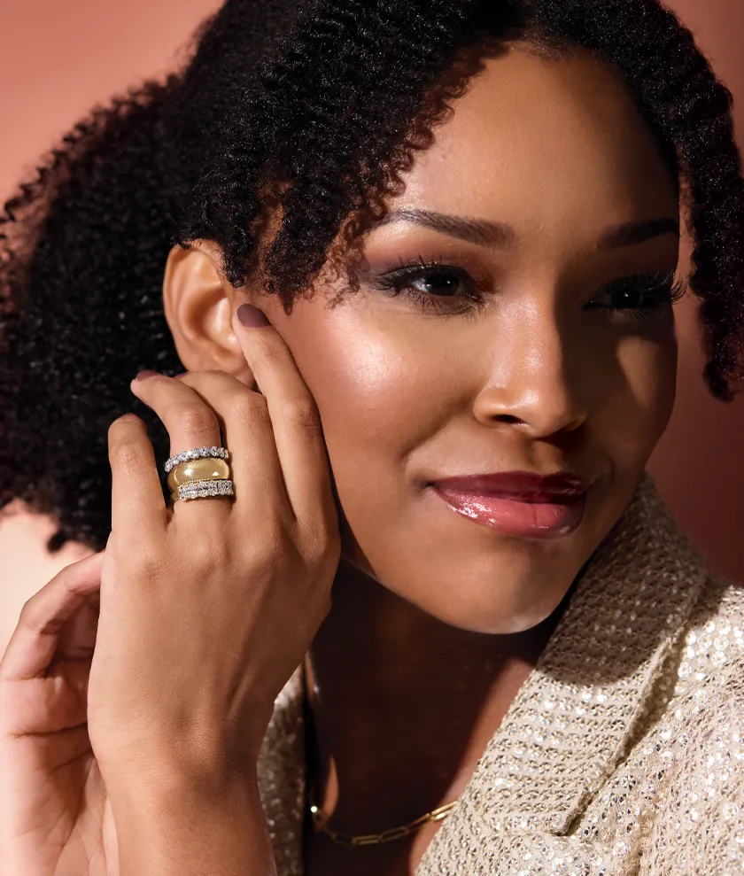 A woman with curly hair showcases a stunning ring, smiling against a warm, soft background.