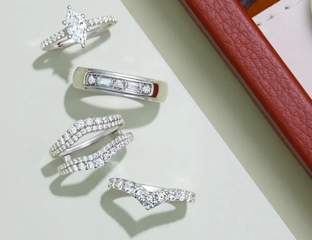 Five elegant diamond rings displayed on a light surface, showcasing various styles.
