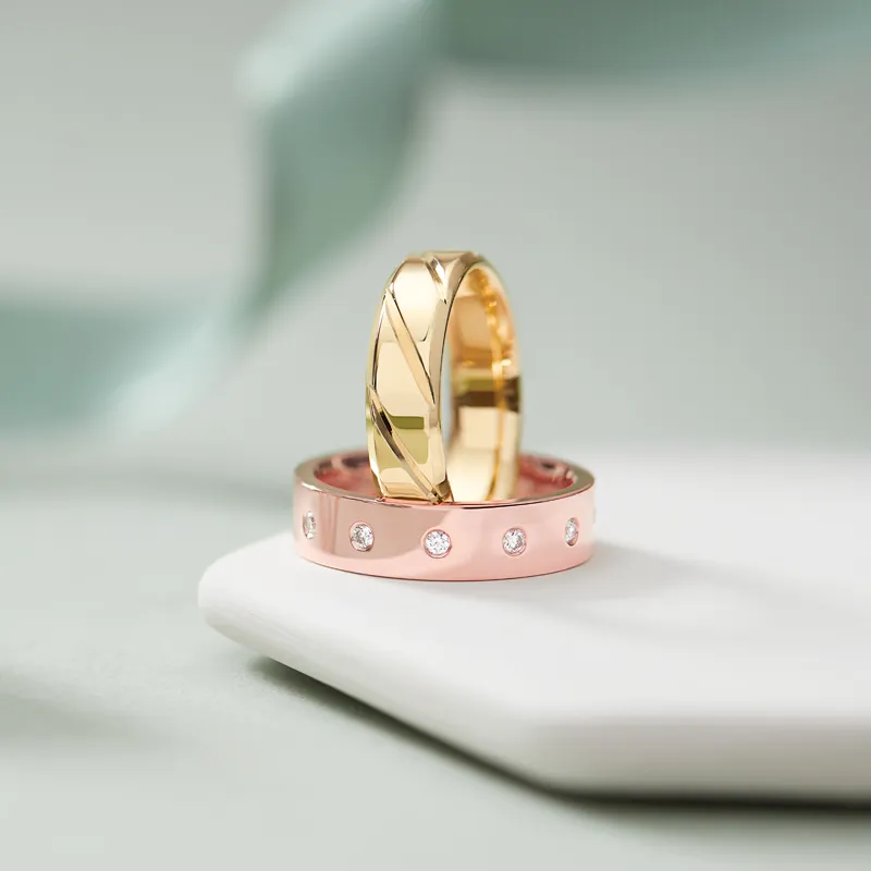 Two elegant rings: a gold band with a twist design and a pink band adorned with diamonds, displayed on a white surface.