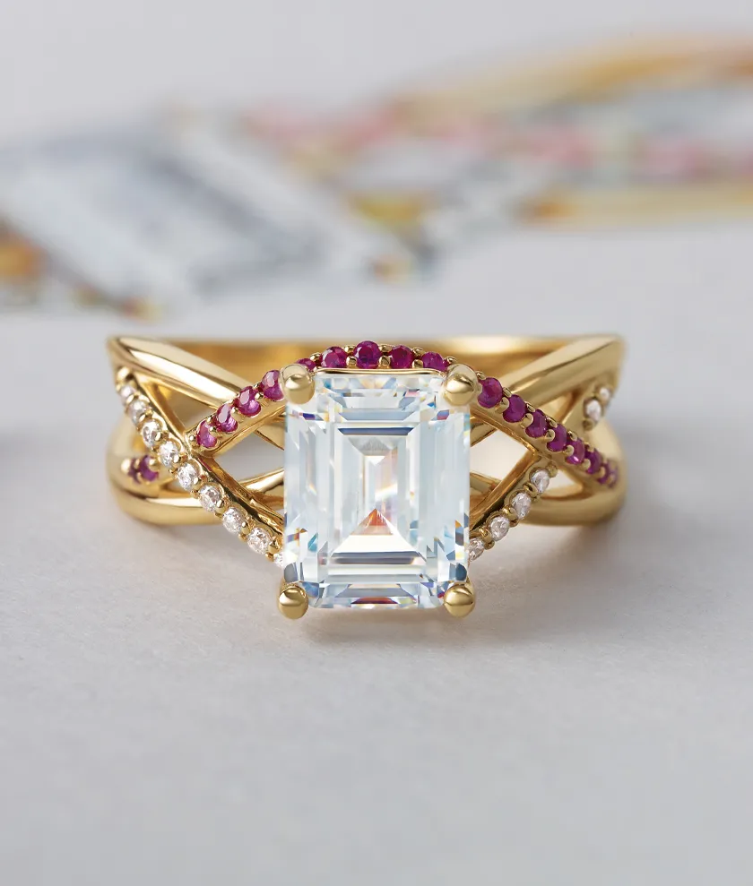Elegant gold ring with a large emerald-cut diamond and ruby accents, alongside a paintbrush on a design sketch.