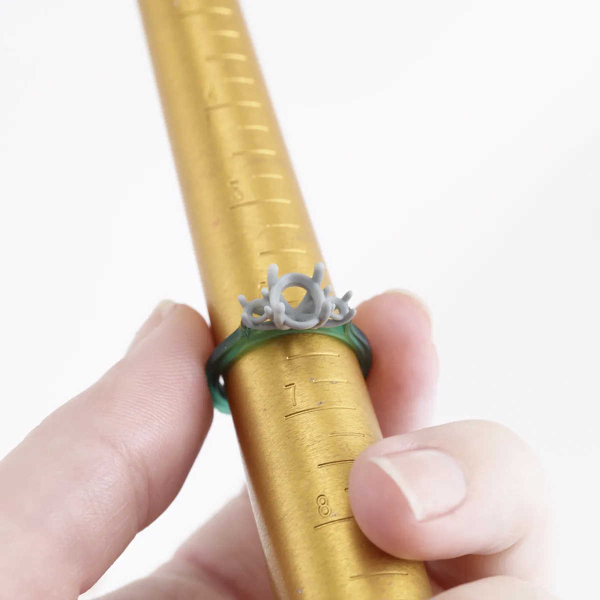 A hand holding a gold ring sizer with a custom gray ring displayed on it.