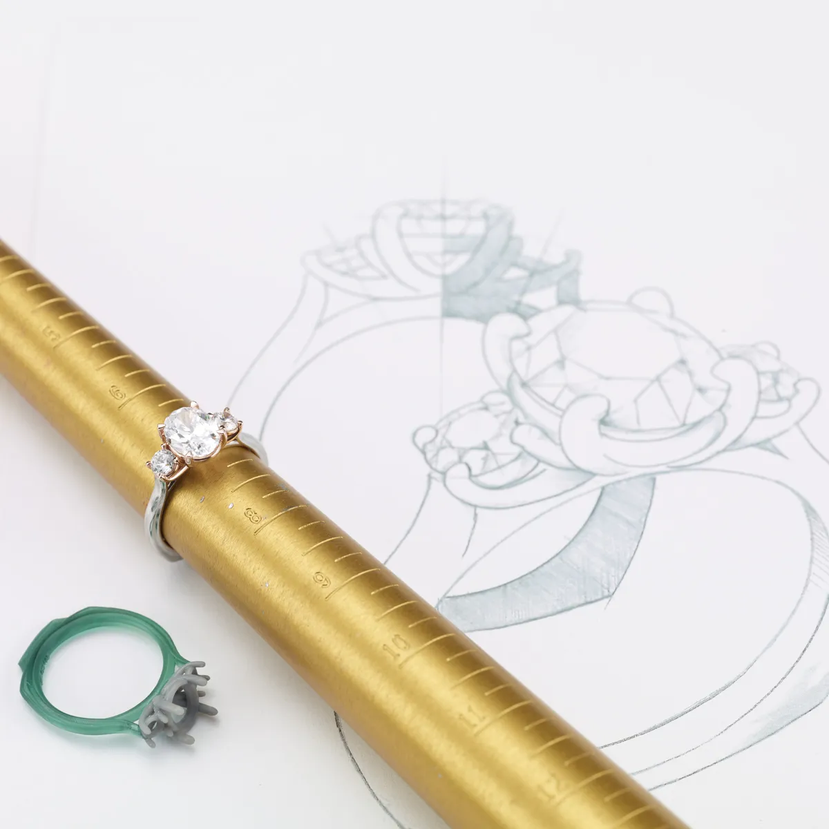 Custom engagement ring on a sizing mandrel with a design sketch in the background.