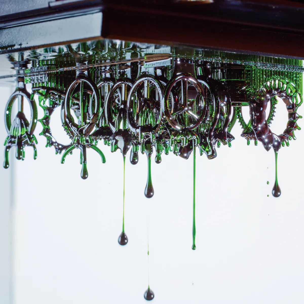 Dripping green liquid forms intricate jewelry shapes, reflecting light in a creative display. 
