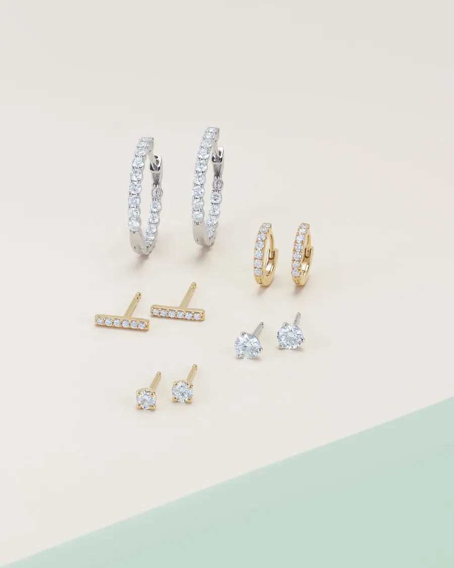 Set of elegant earrings including silver and gold hoops, studs, and bars with sparkling stones.