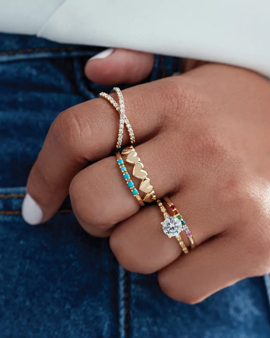 Close-up of multiple gold rings with colorful stones and a diamond, showcasing a stylish hand.