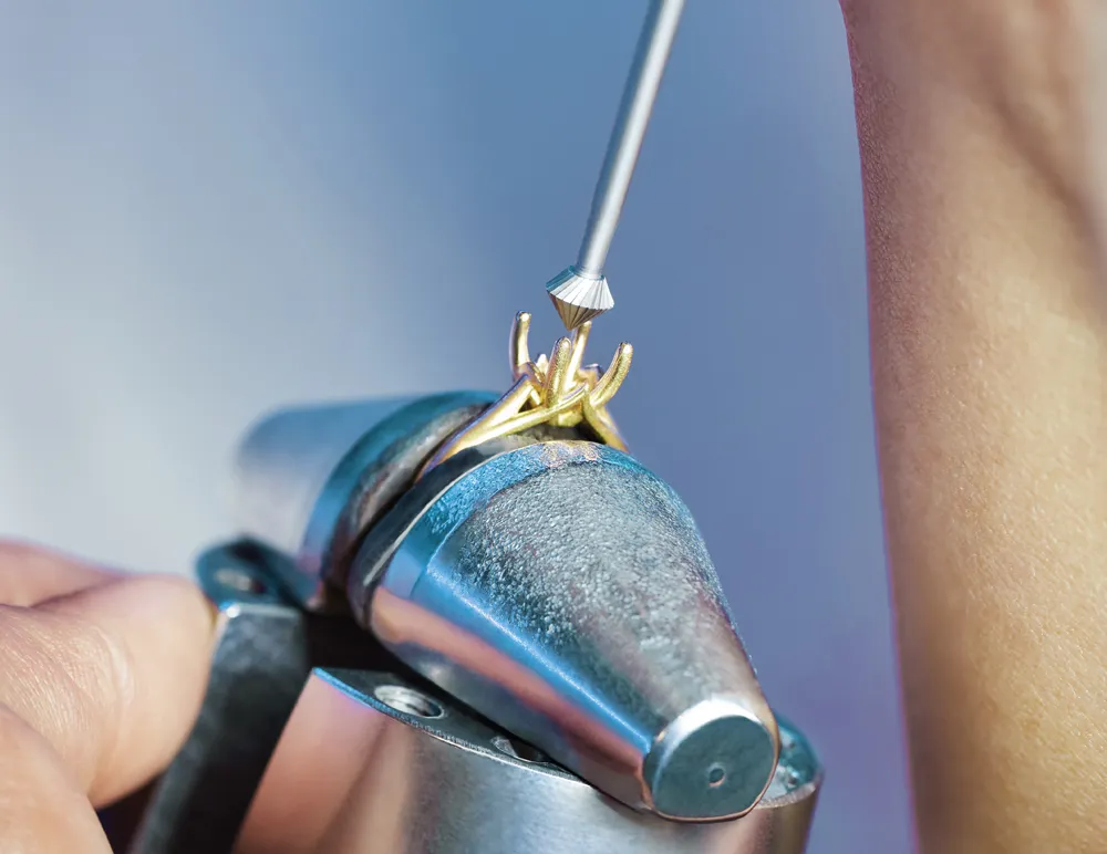 Jeweler working on a gold ring with a tool, showcasing custom jewelry services.