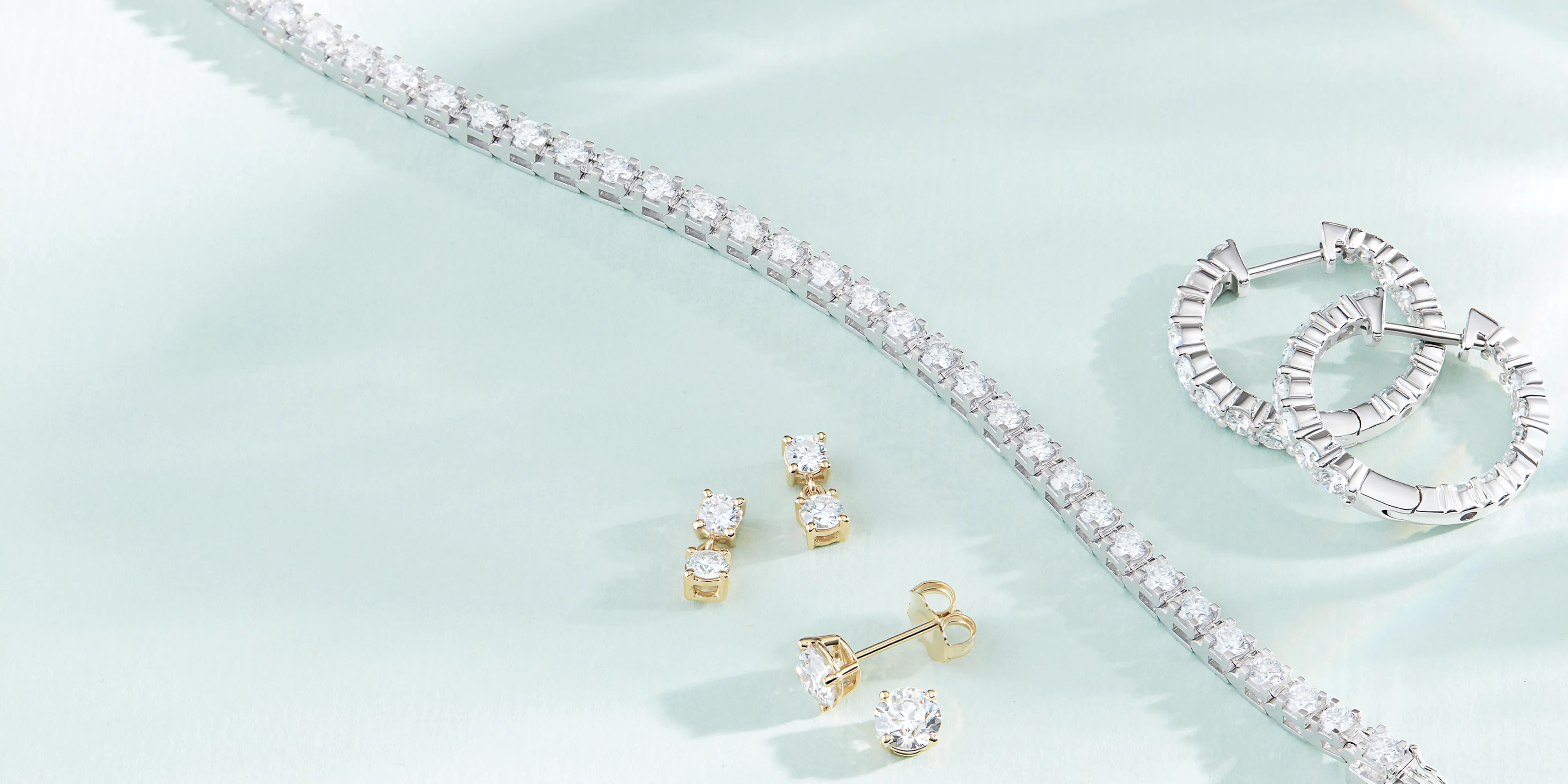 Elegant jewelry display featuring a diamond bracelet, gold and diamond earrings, and silver hoop earrings.