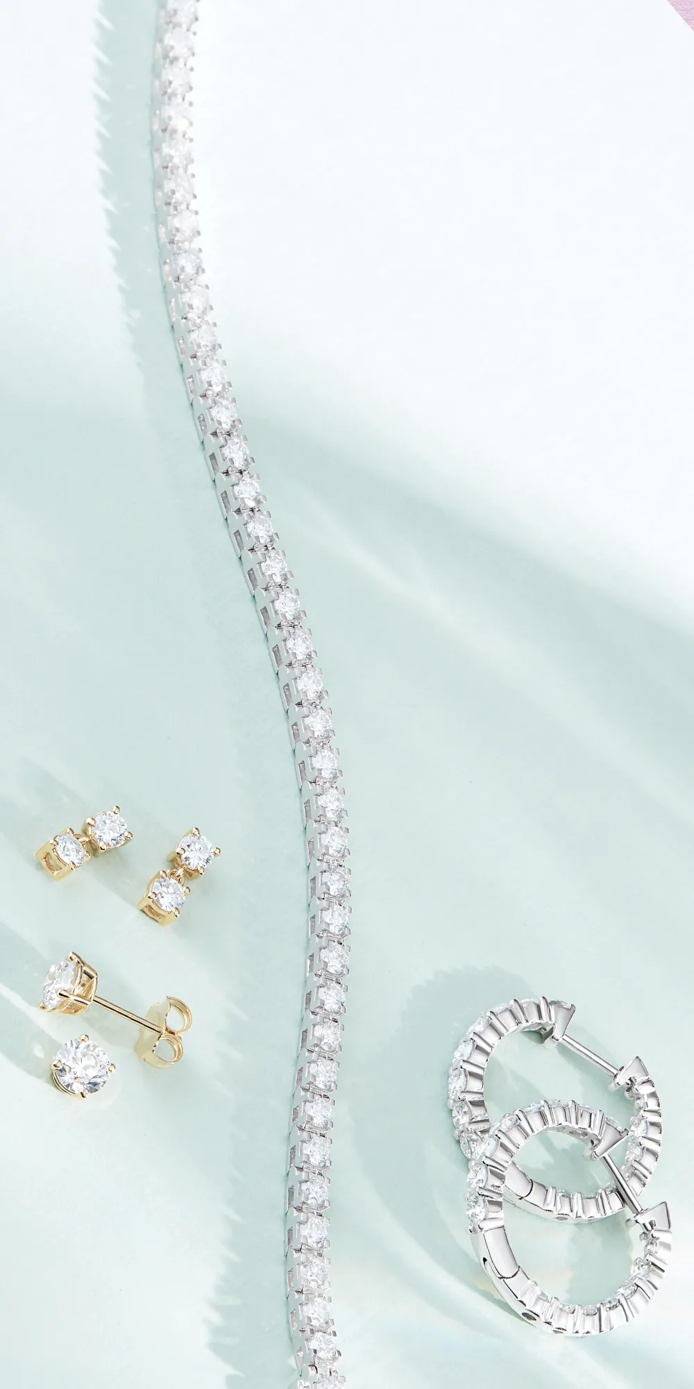 Elegant jewelry display featuring a diamond bracelet, gold and diamond earrings, and silver hoop earrings.
