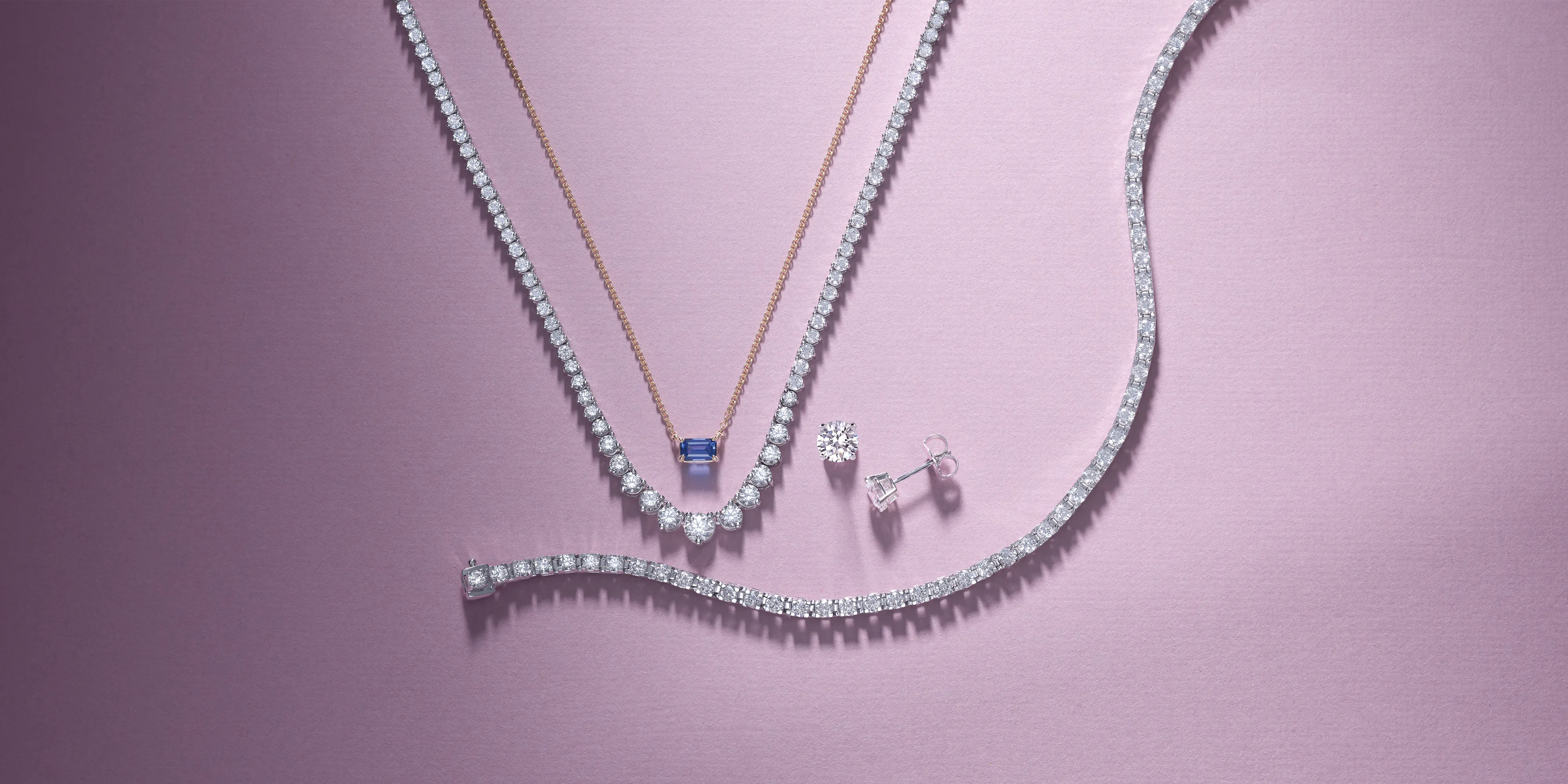 Elegant jewelry display featuring diamond necklaces and earrings on a soft pink background.