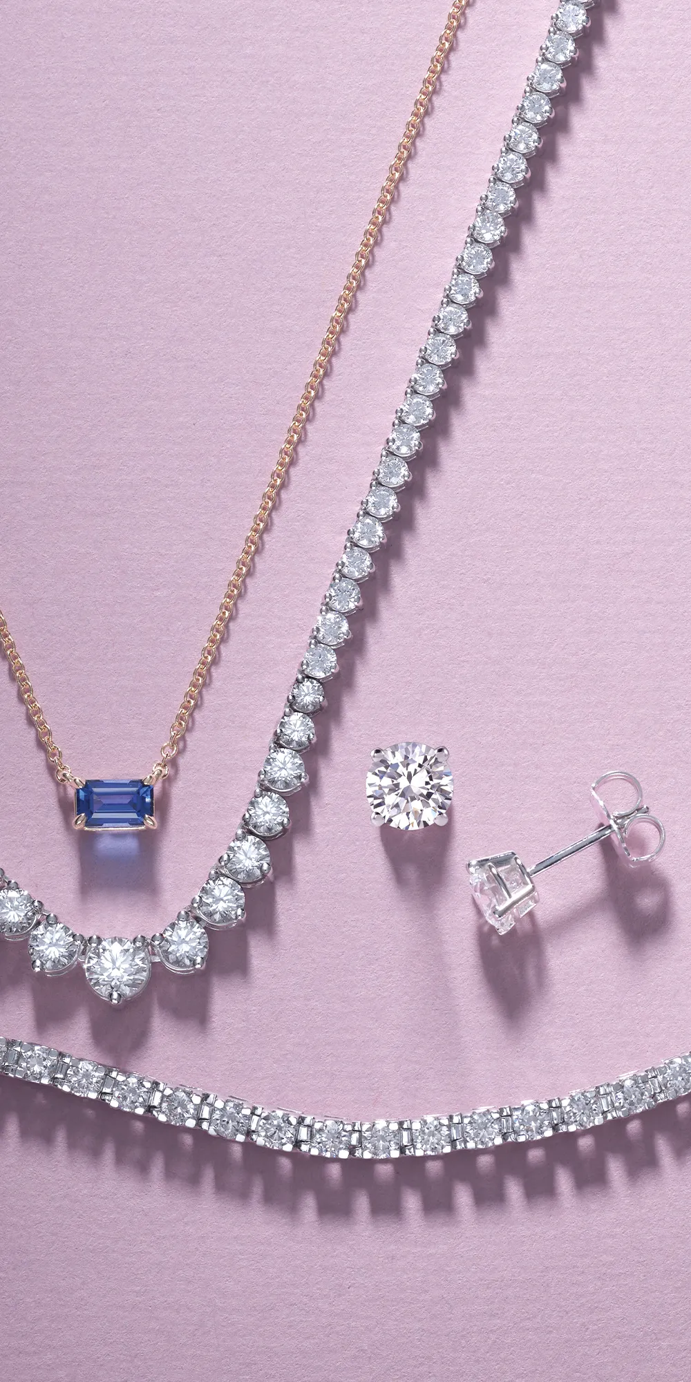 Elegant jewelry display featuring diamond necklaces and earrings on a soft pink background.
