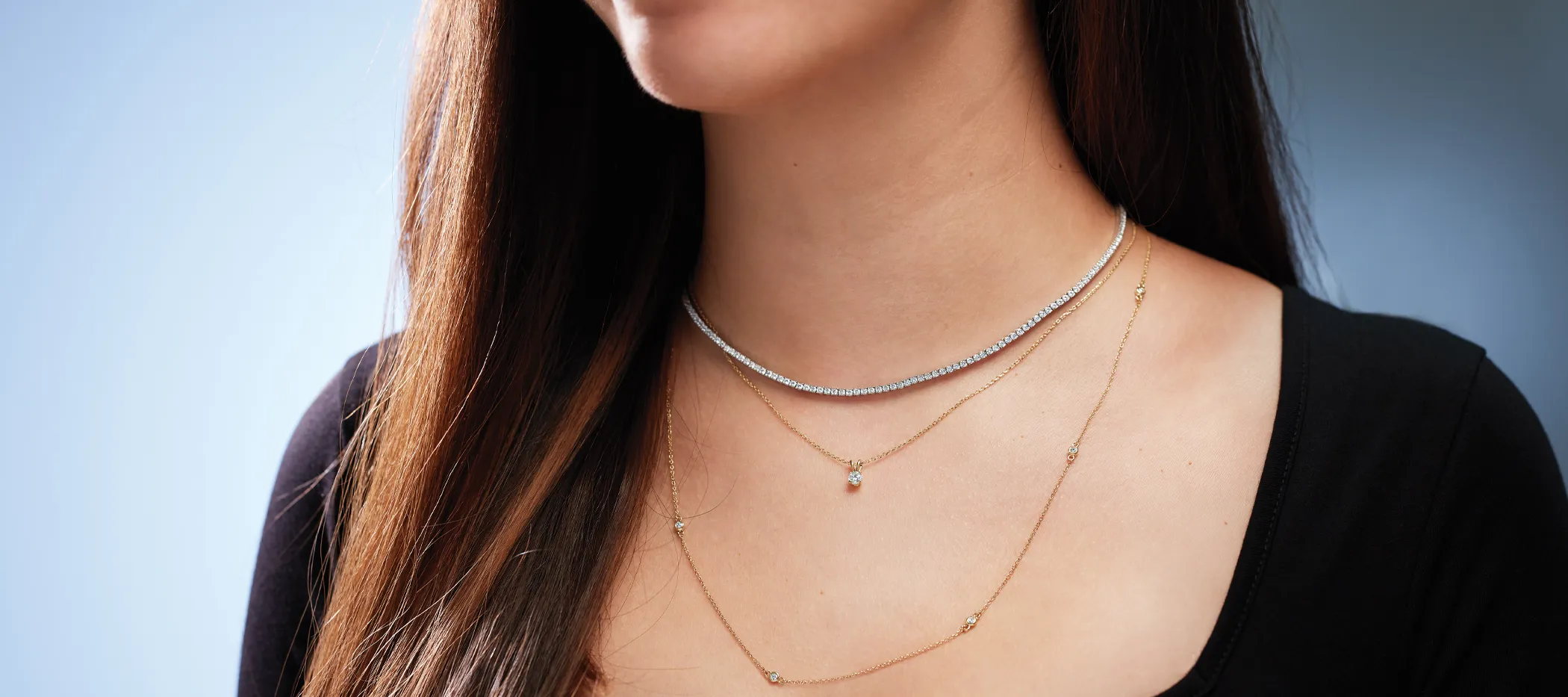 Model wearing layered silver and gold necklaces, showcasing fine jewelry.