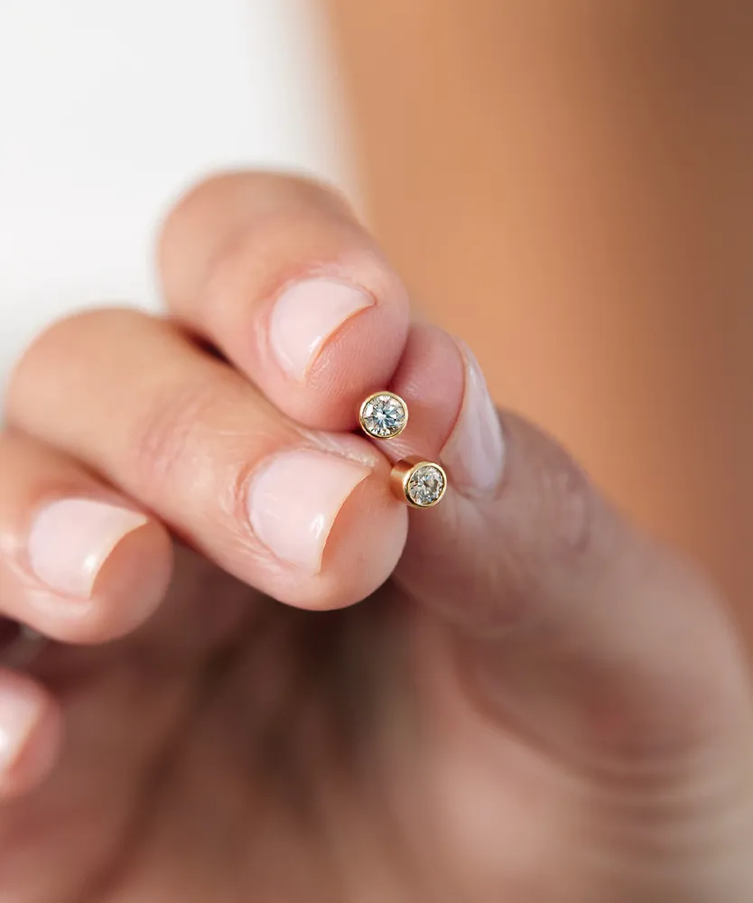 A hand holding two diamond stud earrings set in gold. 