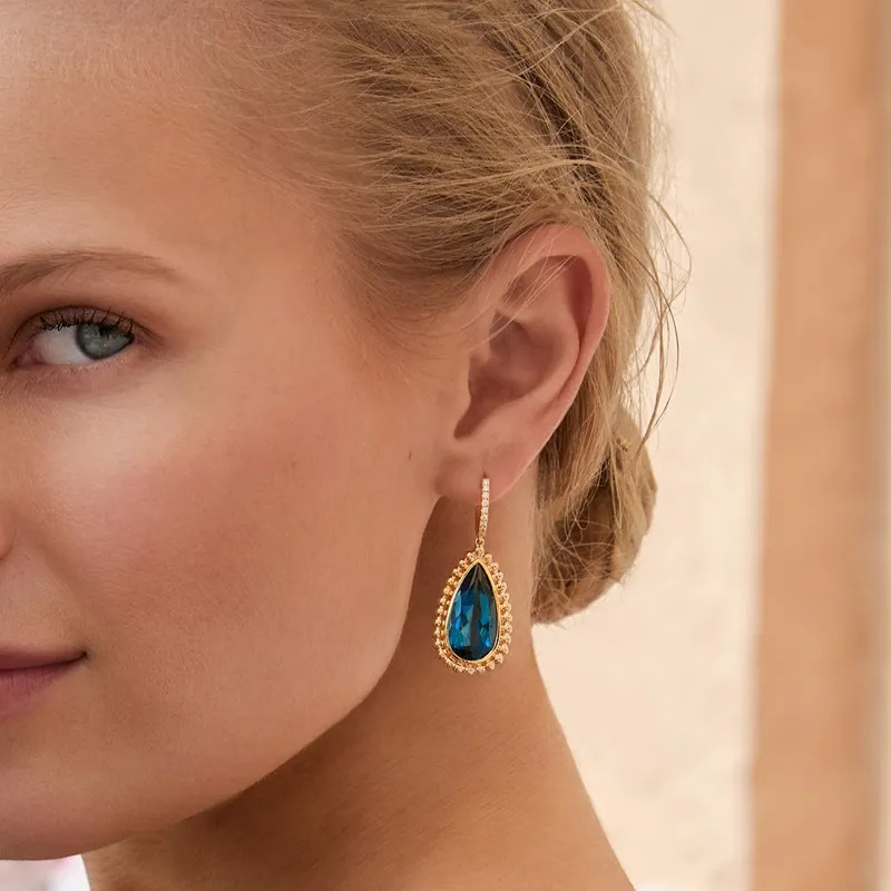 Close-up of a woman wearing a gold teardrop earring with a blue gemstone. 