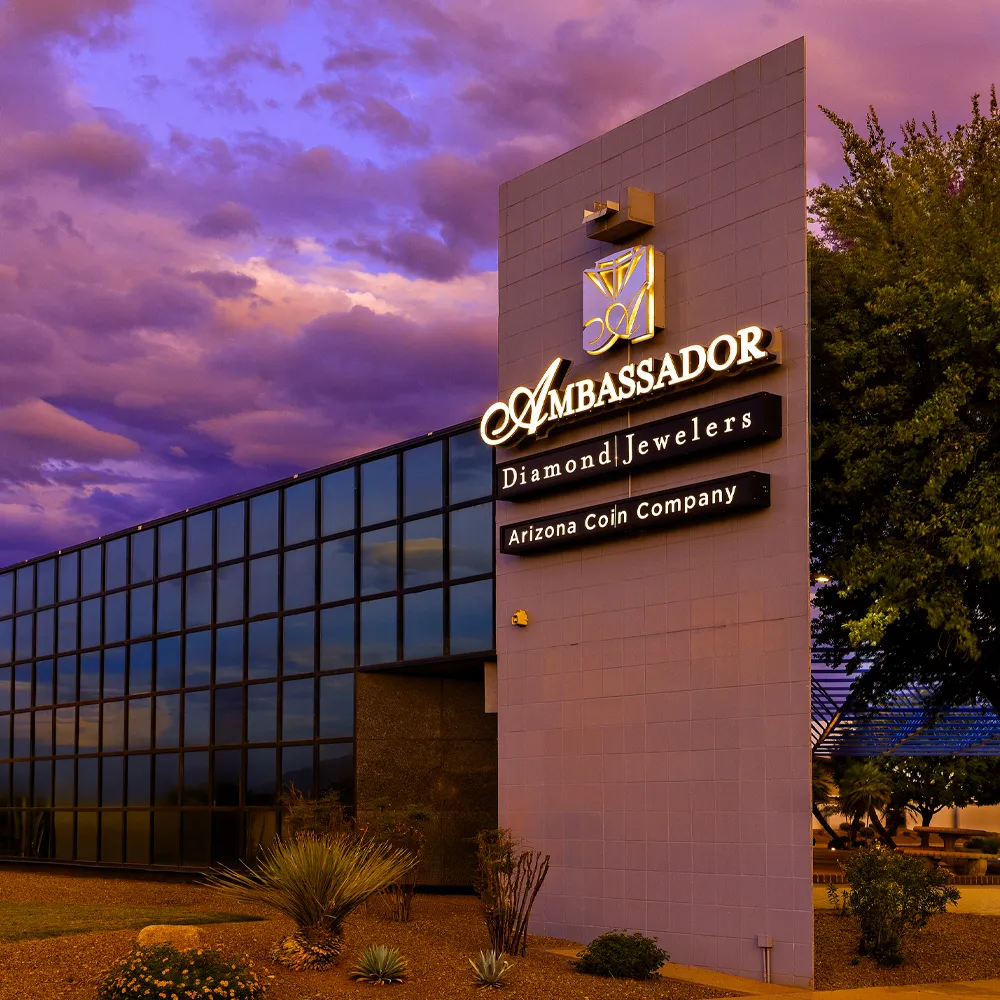 Ambassador Diamond Jewelers storefront in Tucson, showcasing fine jewelry and engagement rings under a colorful sky.