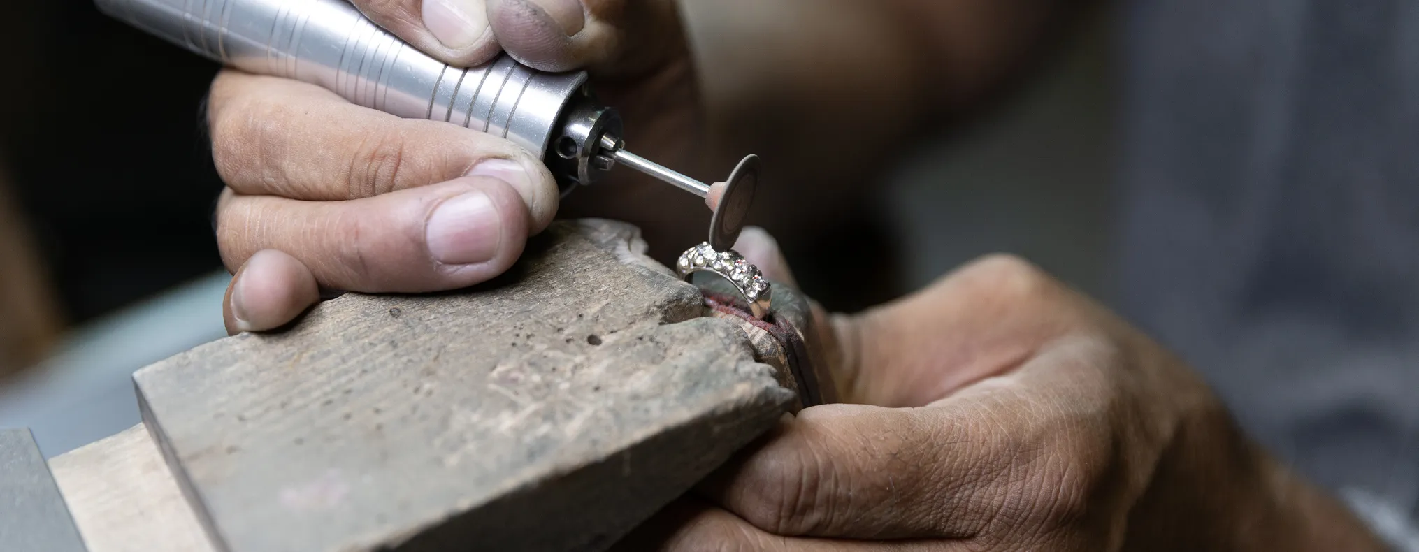 A jeweler meticulously crafts a ring using a rotary tool, showcasing the art of personalized engagement ring design.