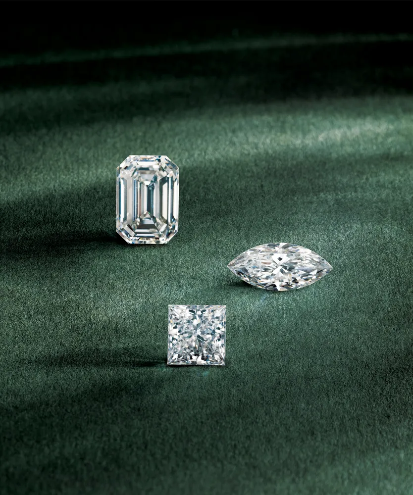Three stunning diamonds on a green background: an emerald cut, a marquise cut, and a princess cut.