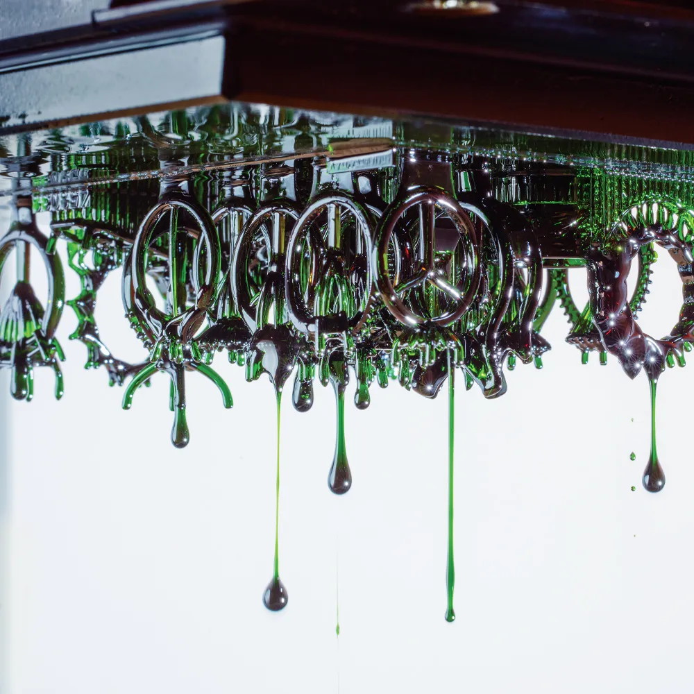 Green liquid drips from silver rings reflecting in a surface, creating an artistic and abstract visual effect.