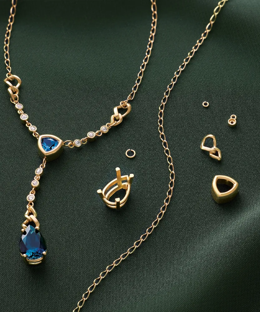 Gold necklace with blue gemstone and diamonds, alongside various jewelry components on a green fabric background.