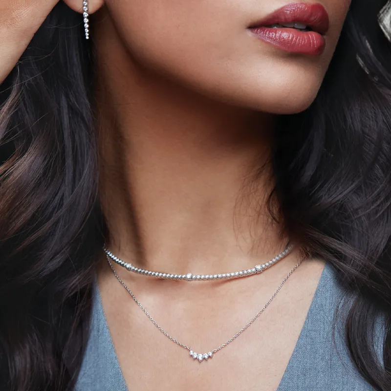 Close-up of a woman wearing layered silver necklaces and earrings, showcasing elegant jewelry.