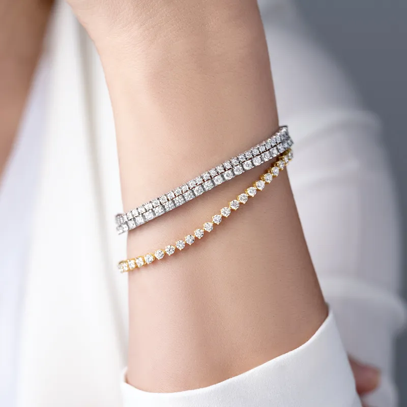 Three elegant tennis bracelets featuring sparkling diamonds and gold accents on a wrist.