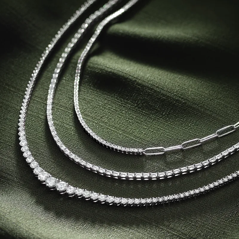 Three elegant diamond tennis necklaces displayed on a green fabric background. 