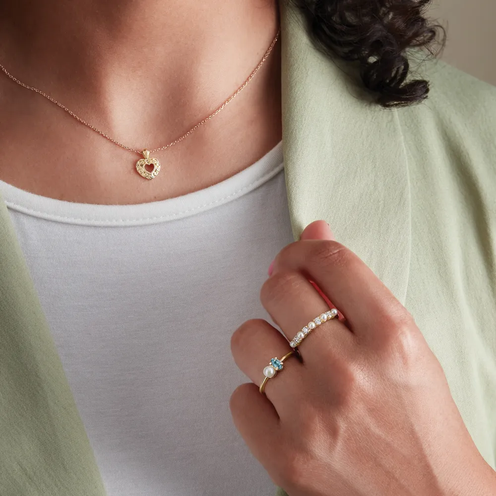 Close-up of a woman wearing a heart pendant necklace and two rings, showcasing fine jewelry from Ambassador Diamond Jewelers.