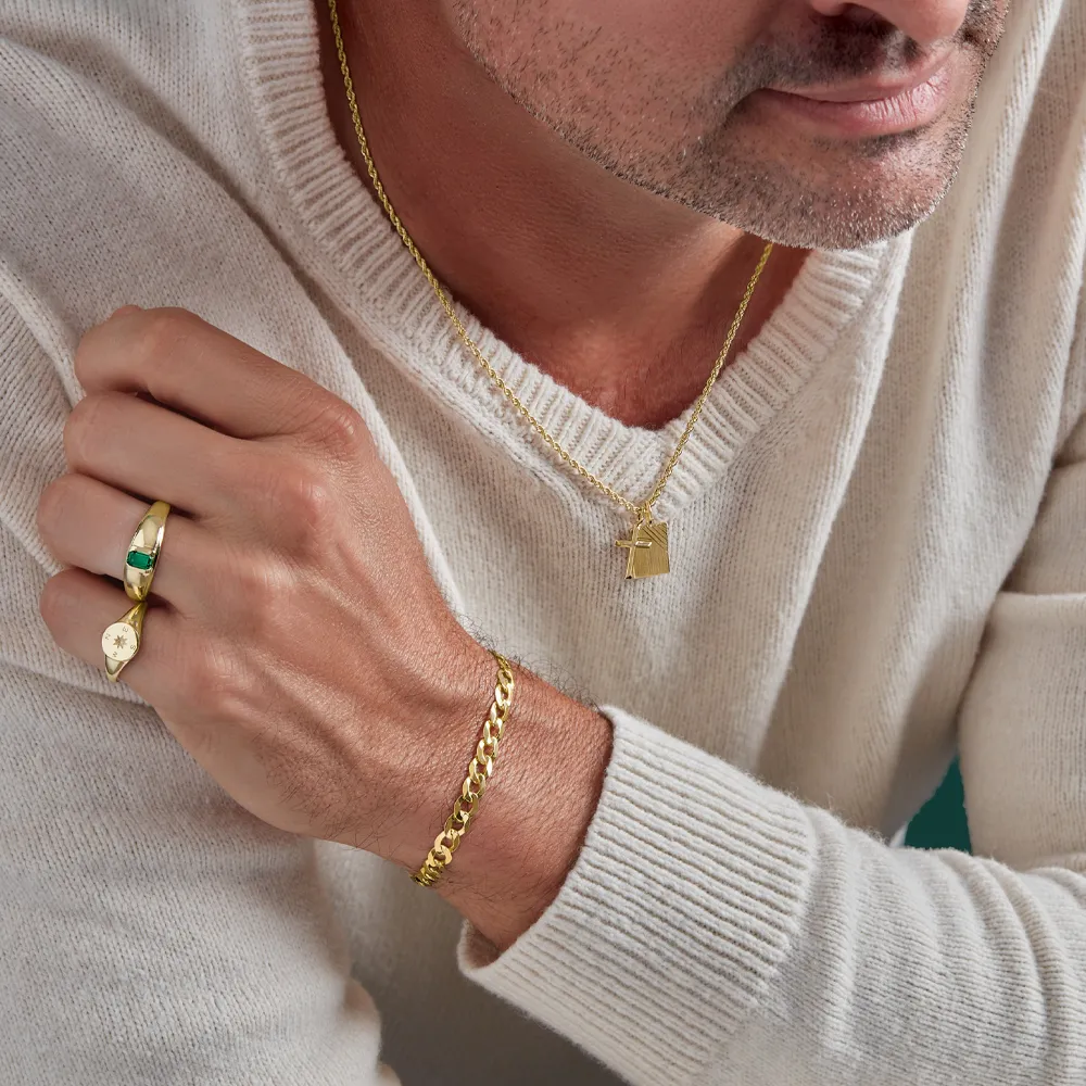 A man wearing gold jewelry, including a necklace, bracelet, and rings, against a neutral background.