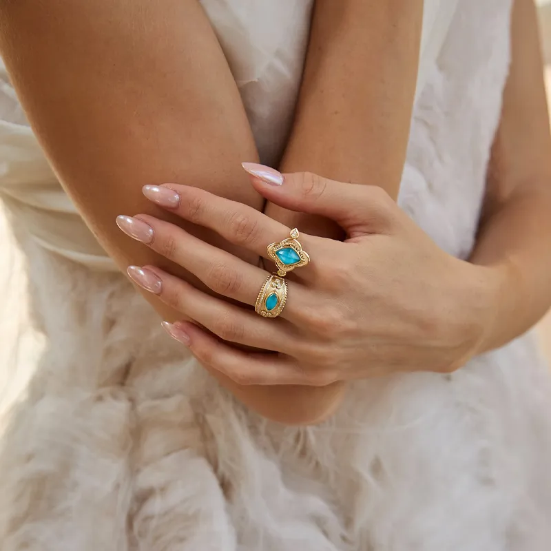 Elegant hands showcasing two gold rings with turquoise stones, perfect for jewelry lovers.