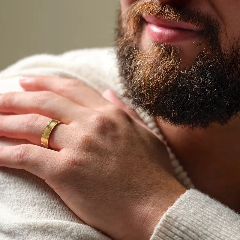 Close-up of a man’s hand with a gold wedding band, resting on his shoulder, showcasing a well-groomed beard.