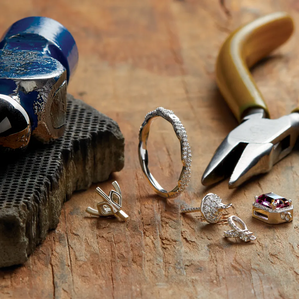 Jewelry tools and pieces including rings and earrings on a wooden surface, showcasing craftsmanship at Amos Jewelry in Wray.