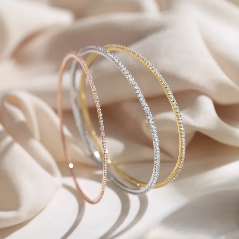 Three elegant bracelets in rose gold, silver, and yellow gold with sparkling accents, displayed on soft fabric.