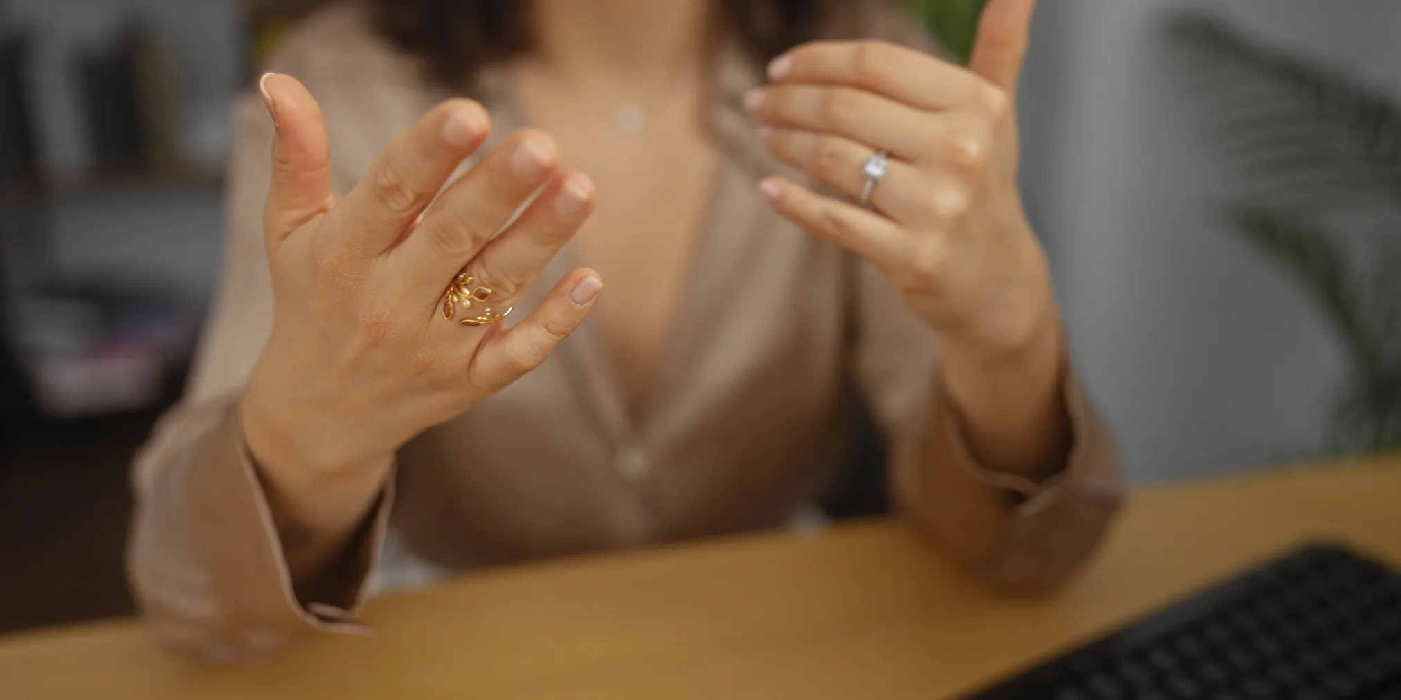 A woman gesturing with her hands, wearing rings, in a professional setting, possibly discussing jewelry. Book an appointment wit