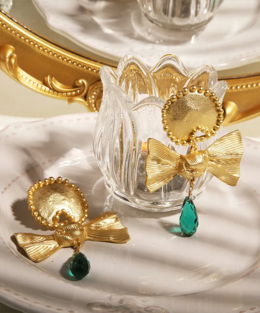 Gold bow earrings with green gemstone accents displayed on a decorative plate, reflecting elegance and style.