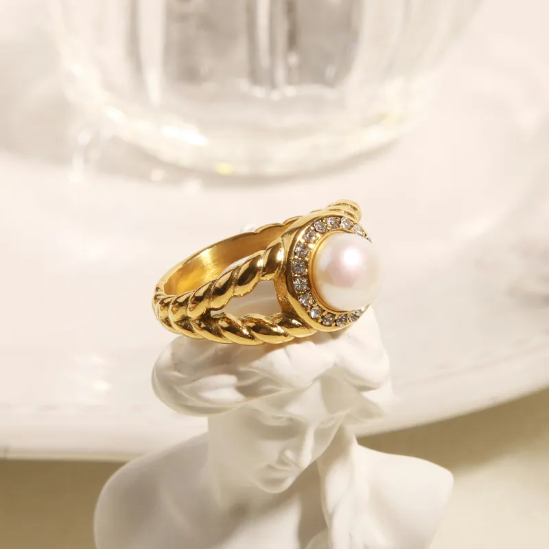 Gold twisted ring featuring a central pearl surrounded by sparkling stones, displayed on a decorative plate.